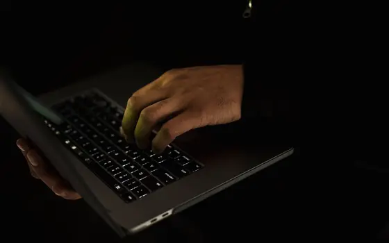 Dłonie piszące na klawiaturze laptopa w ciemnym pokoju
