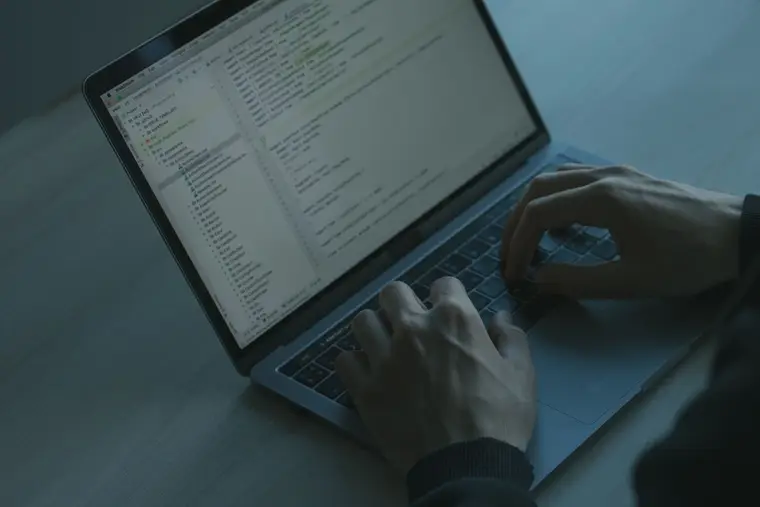 Dłonie przy laptopie z długim tekstem na ekranie w ciemnym pokoju