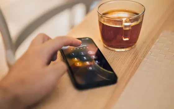 Dłoń wpisująca kod PIN na ekranie telefonu, obok szklanka herbaty