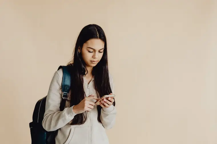 Uczennica z plecakiem patrzy w telefon
